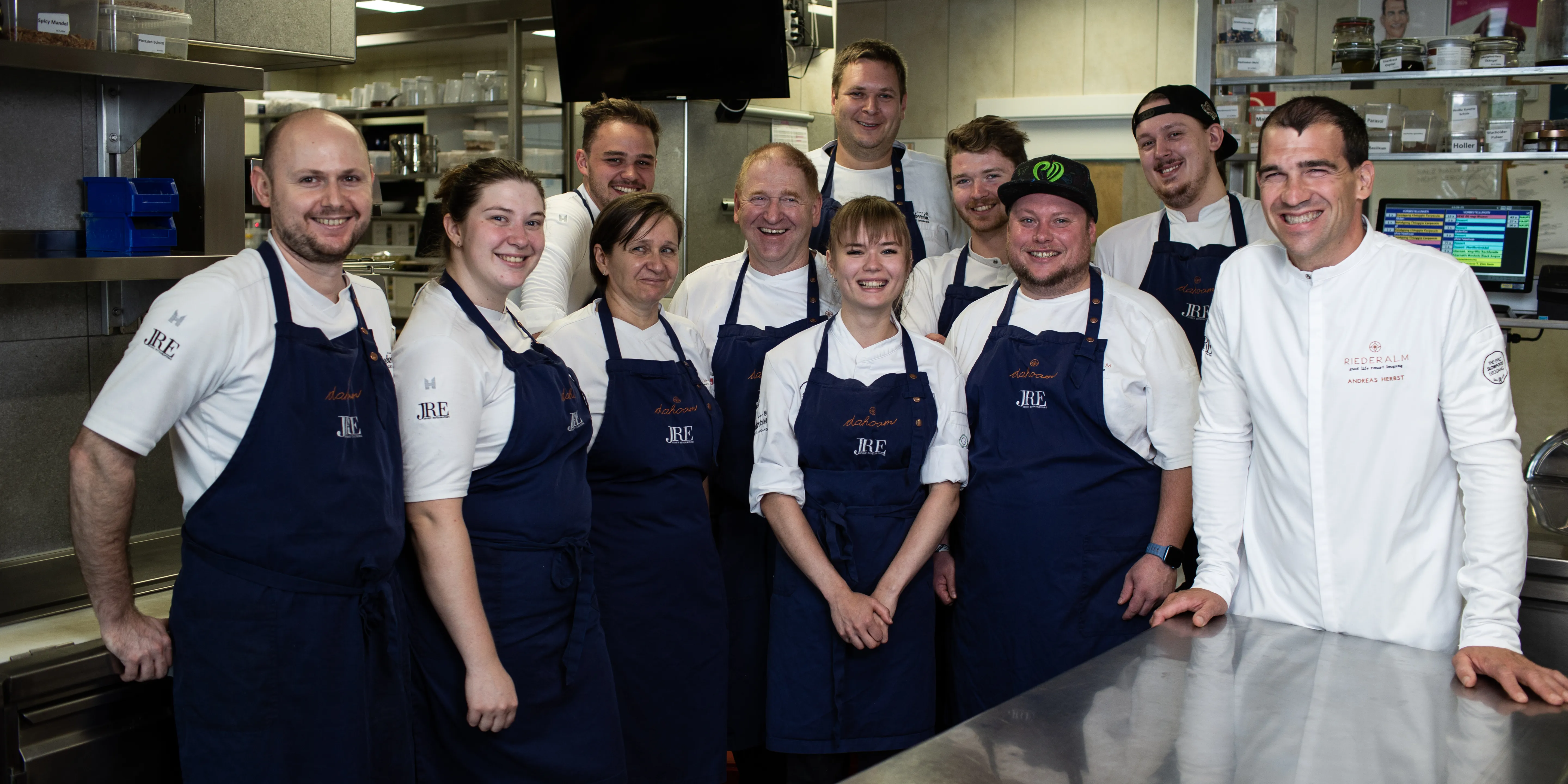 Team of chefs in blue aprons posing together in a professional restaurant kitchen